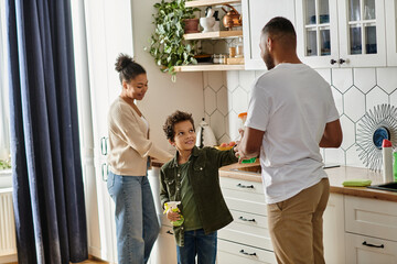 An African American man and woman clean with a child in a cozy kitchen.