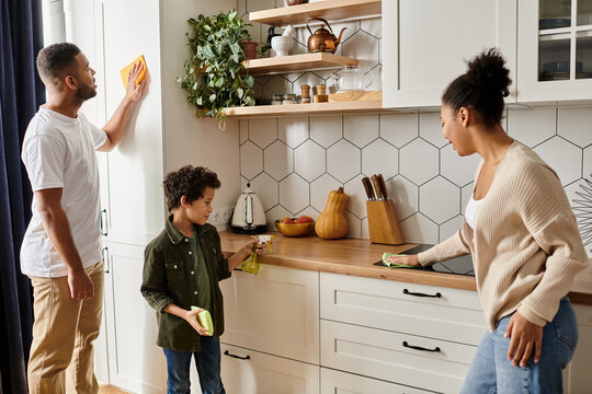 An African American man and woman are energetically cleaning the kitchen together, showing love and teamwork, with son. - Powered by Adobe