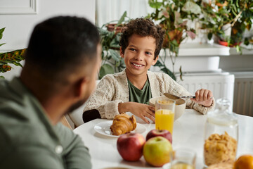 A man and a young boy sit at a table, enjoying a meal together.