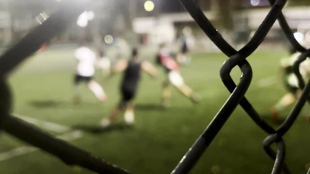 Green field with a fence and net, perfect for playing grass sports. Background football game with metal soccer mesh for competition. Texture and ball goals outdoors, marked lines in the park. Stadium
