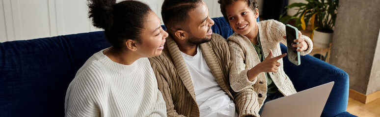 Three people, a loving African-American family, sit on a couch, engrossed in a laptop.
