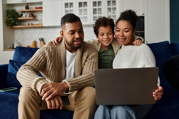 Man, woman, and child watch laptop on couch.