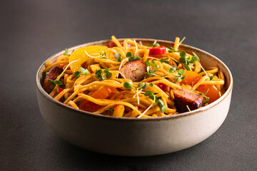 Stir fry noodles with teriyaki sause, vegetables, meat and spices in light ceramic bowl on black background close up. Traditional Asian food concept.