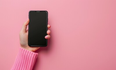 Young adult woman hand holding smartphone and touching black screen with finger on light pink table background. Pastel color. Empty place for text.