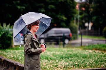 Young woman wearing a pink top and green jacket, smiling while holding a transparent umbrella on a...