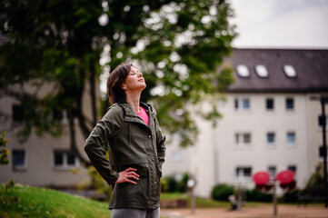 Young woman in a green jacket, standing outdoors on a rainy day with a thoughtful expression. The...