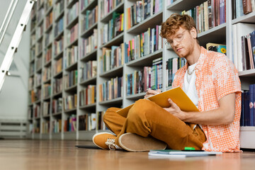 A man engrossed in reading a book while sitting on the floor.