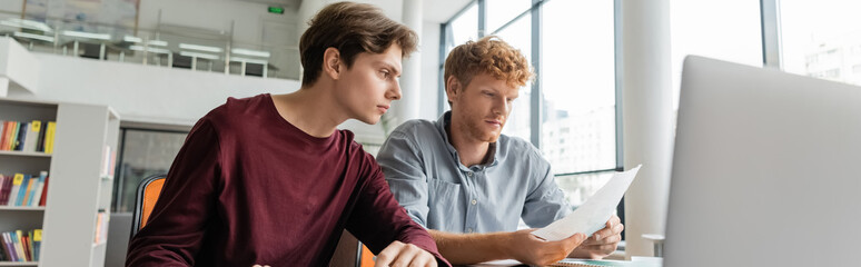 Two men engrossed in studying together at a computer screen in a library.