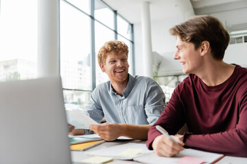 Two young men sitting at a table, focused on studying together using a laptop.