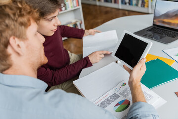 Two students engaged in focused study on a laptop at a table in a library.