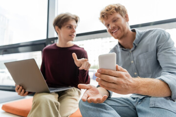 Two male students engrossed in a cell phone while sitting on a couch.