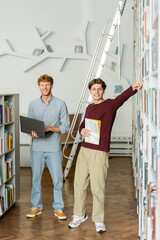 Two young men engrossed in exploration, standing by a library ladder.