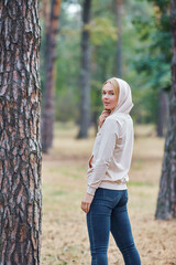 Attractive blue eyed blonde woman walk on the city park. Girl wear beige hoodie, pink bag and look...