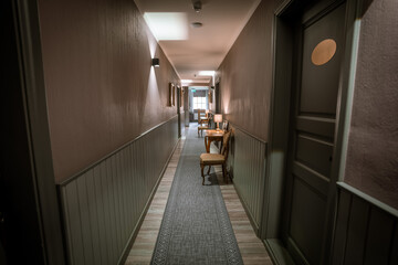 Blome, Latvia - September 11, 2023 - A well-lit, stylish hotel corridor with wooden tables, chairs, lamps, and patterned carpeting, featuring soft ambient lighting.