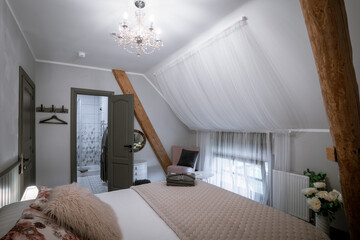 Blome, Latvia - September 11, 2023 - A cozy attic bedroom with a neatly made bed, floral and furry...