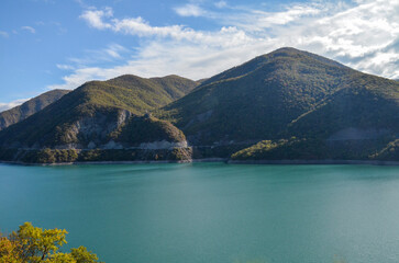 Turquoise water surface reflects the blue sky of Zhinvali Reservoir nestled amidst lush green hills or mountains. Travel to Georgia