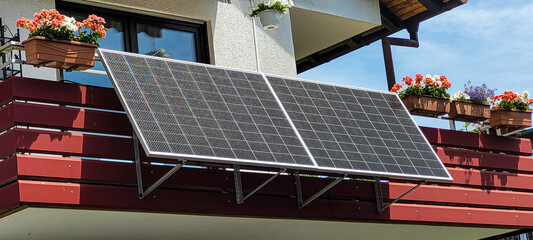 Balcony solar system, fixed at an angle of 30 degrees on the red balcony of an apartment building,...