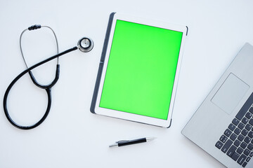 Tablet, green screen and stethoscope on desk in hospital for wellness, app or ui with mock up space. Digital touchscreen, laptop and medical tools for communication, telehealth and services in clinic