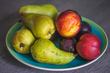 Plate with fresh ripe fruit: pears, nectarine and plums on table; close up