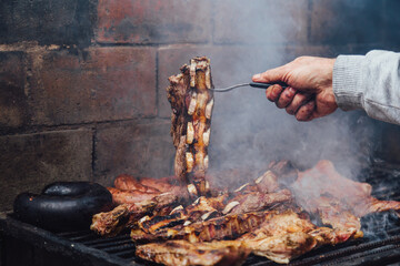 Mature man doing a bbq. He is prodding the meat with a fork. Traditional barbecue called Asado in...
