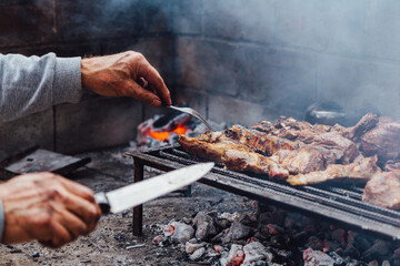 Mature man doing a bbq. He is prodding the meat with a fork. Traditional barbecue called Asado in...