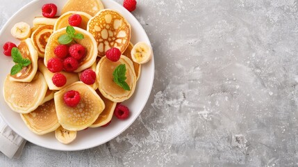 A plate of fluffy pancakes topped with fresh berries, a drizzle of syrup, and a sprig of mint.