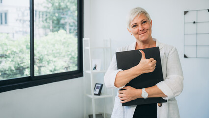 A woman is holding a black folder and giving a thumbs up