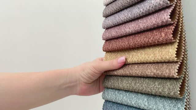 Choosing upholstery fabric samples. Interior designer selecting textile palette. Fabric selection for furniture upholstery. Hand holding fabric swatches. Textile choice for home interior.