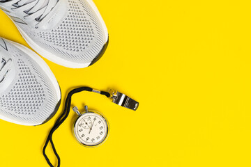 Pair of white sneakers, stopwatch and whistle on yellow background. Sports concept.