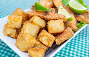 Portion of crunchy breaded deep fried fish in cubes, with lettuce below and lemon on top, on a table, in close-up.