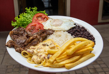 Dish of rice, beans, egg, lettuce, tomato, french fries, grilled steak and pasta with bacon sauce. In Brazil, this dish is called 'Executive dish'. Big plate of food.