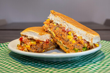 Delicious fresh beef strogonoff burger cut in half, with bread, beef, cheese, tomatoes, lettuce, egg, corns, peas and sauce. This type os food is known as xis in Brazil.