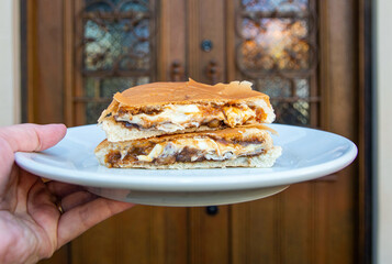 Hand holding plate with typical Brazilian sweet burger, made with bread, cheese, white chocolate...