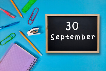 September 30 written in chalk on black board. Calendar date 30th of September on chalkboard on blue blurred school stationery background. Back to school. School event schedule date. Month of autumn.
