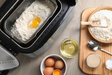 Making dough. Breadmaker and ingredients on wooden table, flat lay