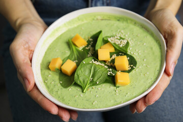 Woman holding bowl of delicious spinach cream soup, closeup