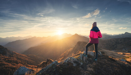 Young woman on mountain peak and beautiful mountain valley in haze at colorful sunset in autumn....