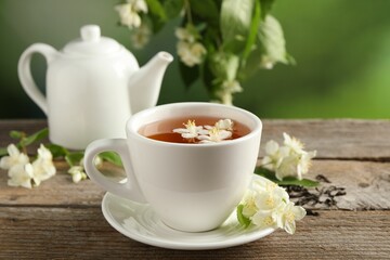 Aromatic jasmine tea in cup, flowers, dry leaves and teapot on wooden table outdoors