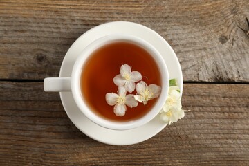 Aromatic jasmine tea in cup and flowers on wooden table, top view