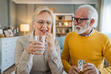 senior couple at home woman take medicine while her husband sit beside