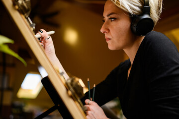 Side view of creative artist with headphones pencil drawing on board.