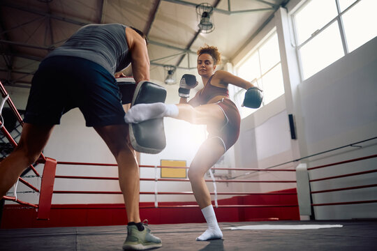 Female fighter practicing leg kick during sports training with her instructor in health club. - Powered by Adobe