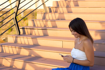 Young attractive woman in blue dress using her smart phone and sitting on stairway