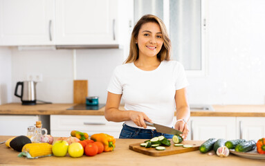 Young smiling woman chopping vegetables in home kitchen, preparing vegan dish