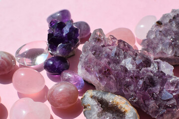Beautiful purple druses and amethyst geodes and rose quartz stones on a pink background. Healing crystals.