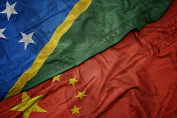 waving colorful flag of Solomon Islands and national flag of china on the dollar money background. finance concept.