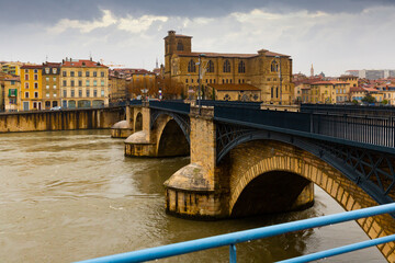 Naklejka premium Scenic view across Isere river of Romans-sur-Isere embankment with St. Barnard Roman Catholic Cathedral and ancient stone arched bridge in winter, France