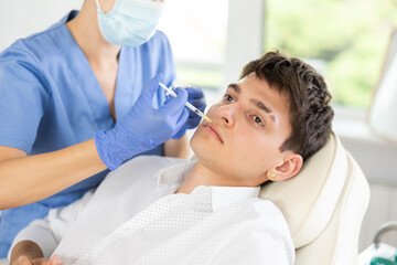 Brunette guy having facial injection at bright treatment room