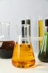Laboratory glassware with different types of oil on white table, closeup