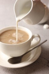 Pouring milk into cup with coffee on light grey textured table, closeup